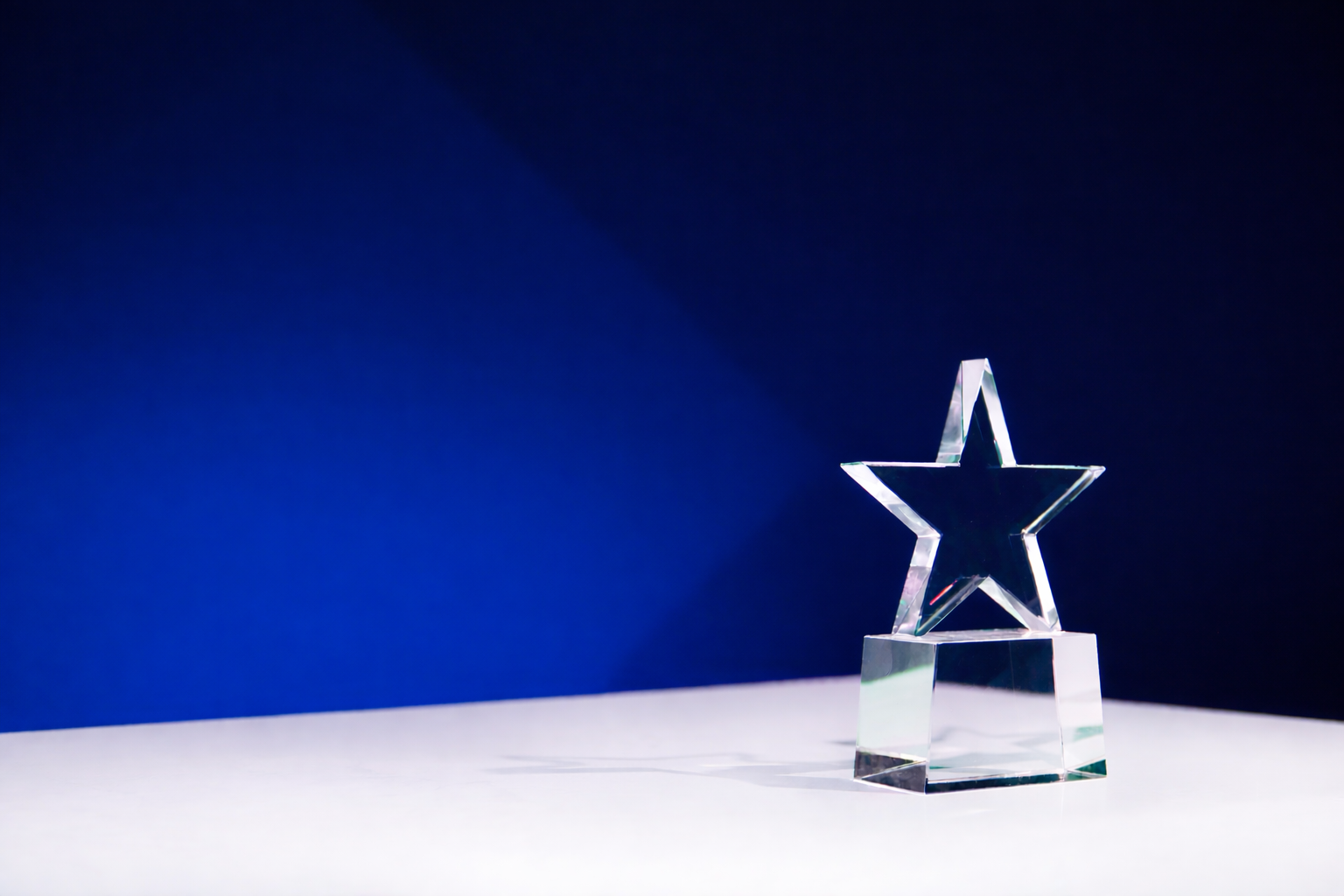 Clear star-shaped trophy on a white surface with a blue background
